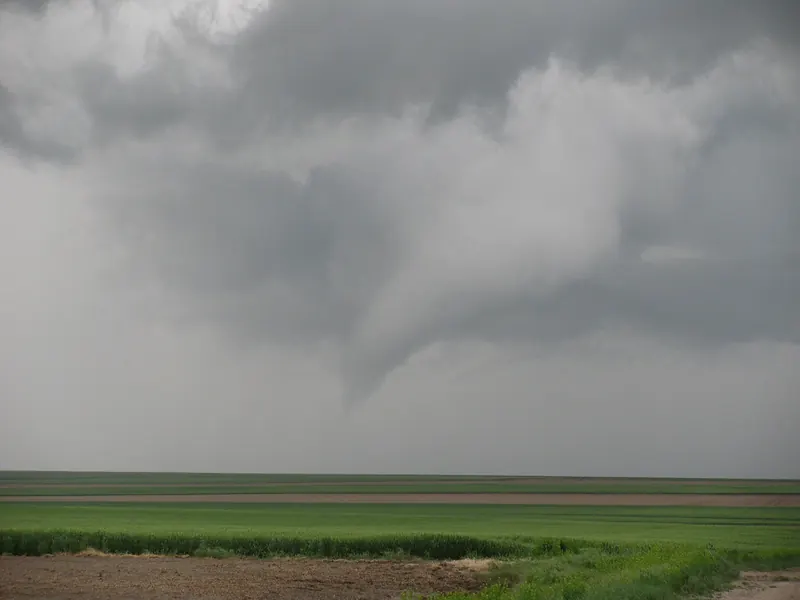 A lowered, ragged storm cloud hanging over flat green farmland