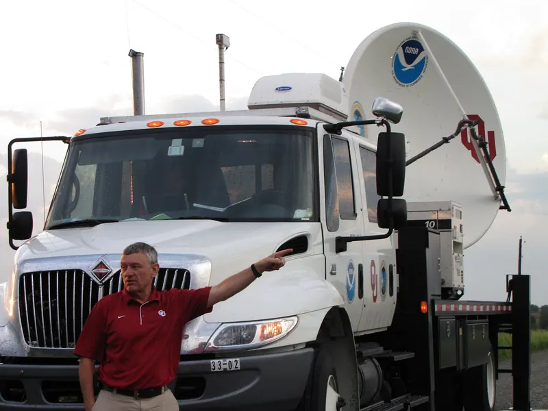A truck with a large radar dish on the back, parked under a stormy sky