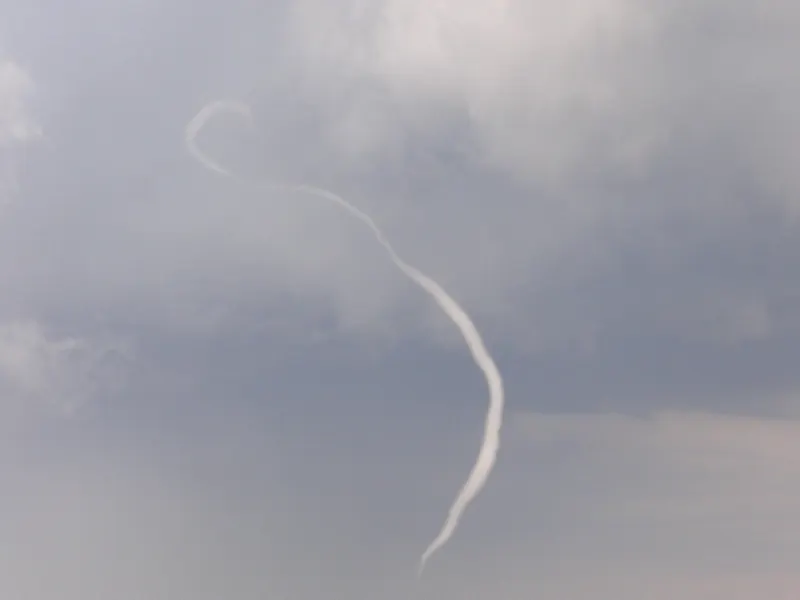 A thin, white, rope-shaped tornado twisting down from a grey sky