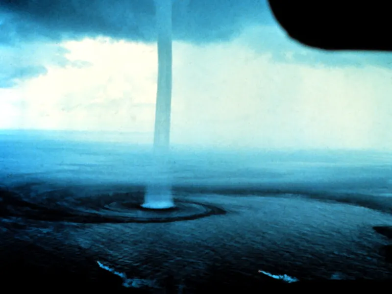A long, thin white waterspout under a cloud base