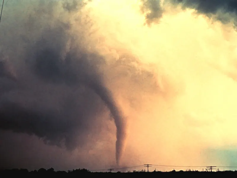 A thin, pale funnel just beginning to reach down from a storm cloud over open land